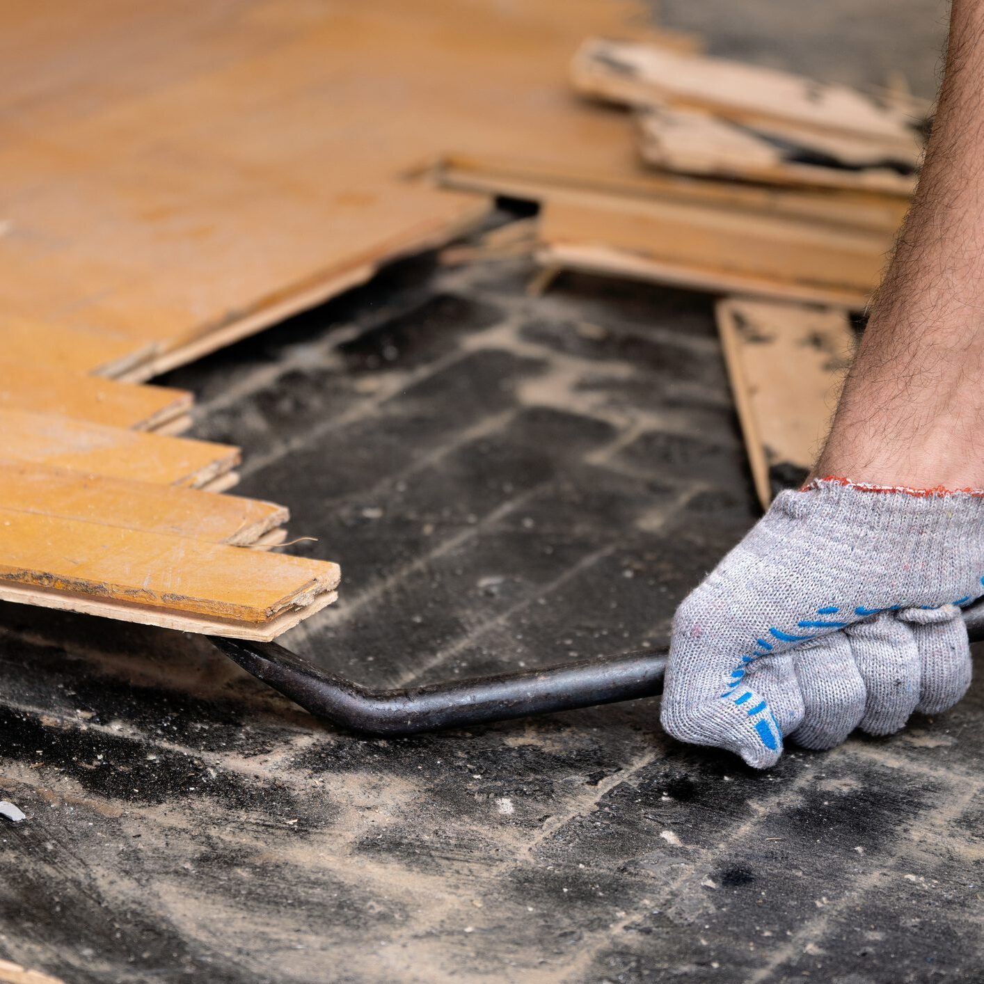 Worker removes old parquet using a tire iron tool during a flat renovation close up